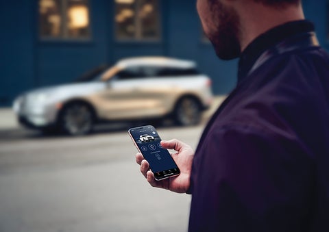 A person is shown interacting with a smartphone to connect to a Lincoln vehicle across the street. | Gary Yeomans Lincoln in Daytona Beach FL