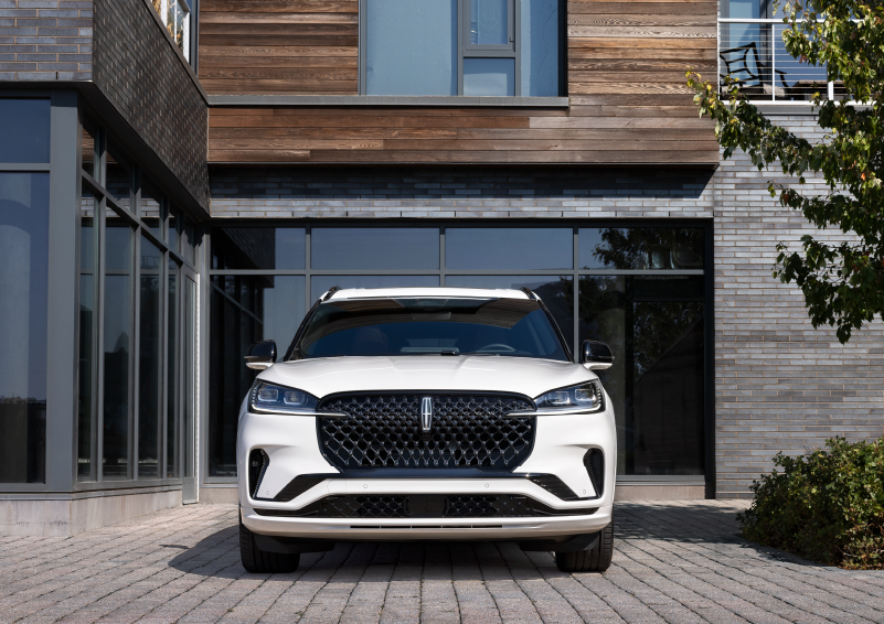 A white 2025 Lincoln Aviator® SUV is shown parked outside a modern building with gray brick and wood accents. | Gary Yeomans Lincoln in Daytona Beach FL