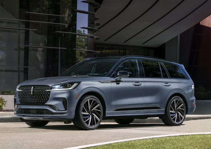 A gray 2025 Lincoln Aviator® SUV is parked outside a modern building showcasing the driver’s side of the vehicle. | Gary Yeomans Lincoln in Daytona Beach FL