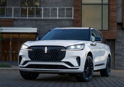 A white 2025 Lincoln Aviator® SUV is shown parked outside a modern building with gray brick and wood accents. | Gary Yeomans Lincoln in Daytona Beach FL