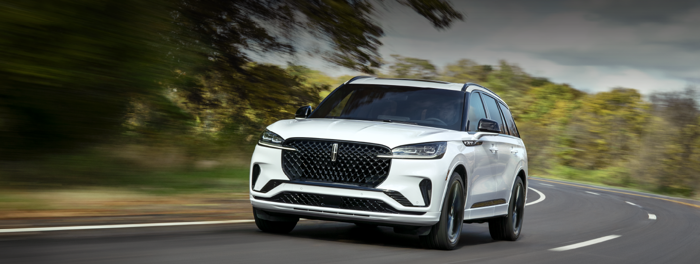 A white 2025 Lincoln Aviator® SUV is being driven down a road lined with trees. | Gary Yeomans Lincoln in Daytona Beach FL