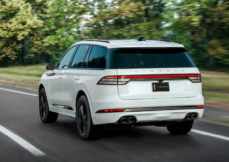 A white 2026 Lincoln Aviator® SUV is being driven away down a road lined with colorful trees. | Gary Yeomans Lincoln in Daytona Beach FL