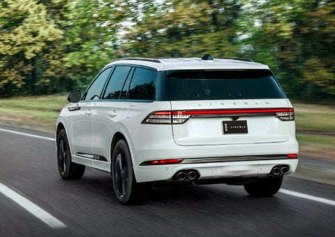 A white 2026 Lincoln Aviator® SUV is being driven away down a road lined with colorful trees. | Gary Yeomans Lincoln in Daytona Beach FL