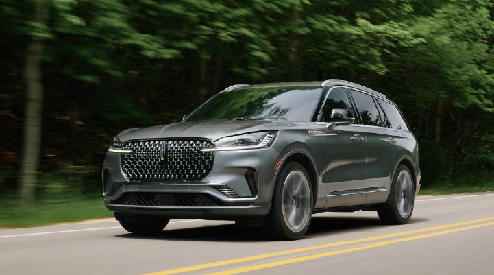 A 2027 Lincoln Aviator® SUV is being driven down a road lined with trees. | Gary Yeomans Lincoln in Daytona Beach FL